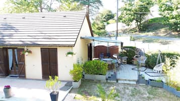 A house with a sloped roof, a patio with outdoor furniture, and a garden area with potted plants.