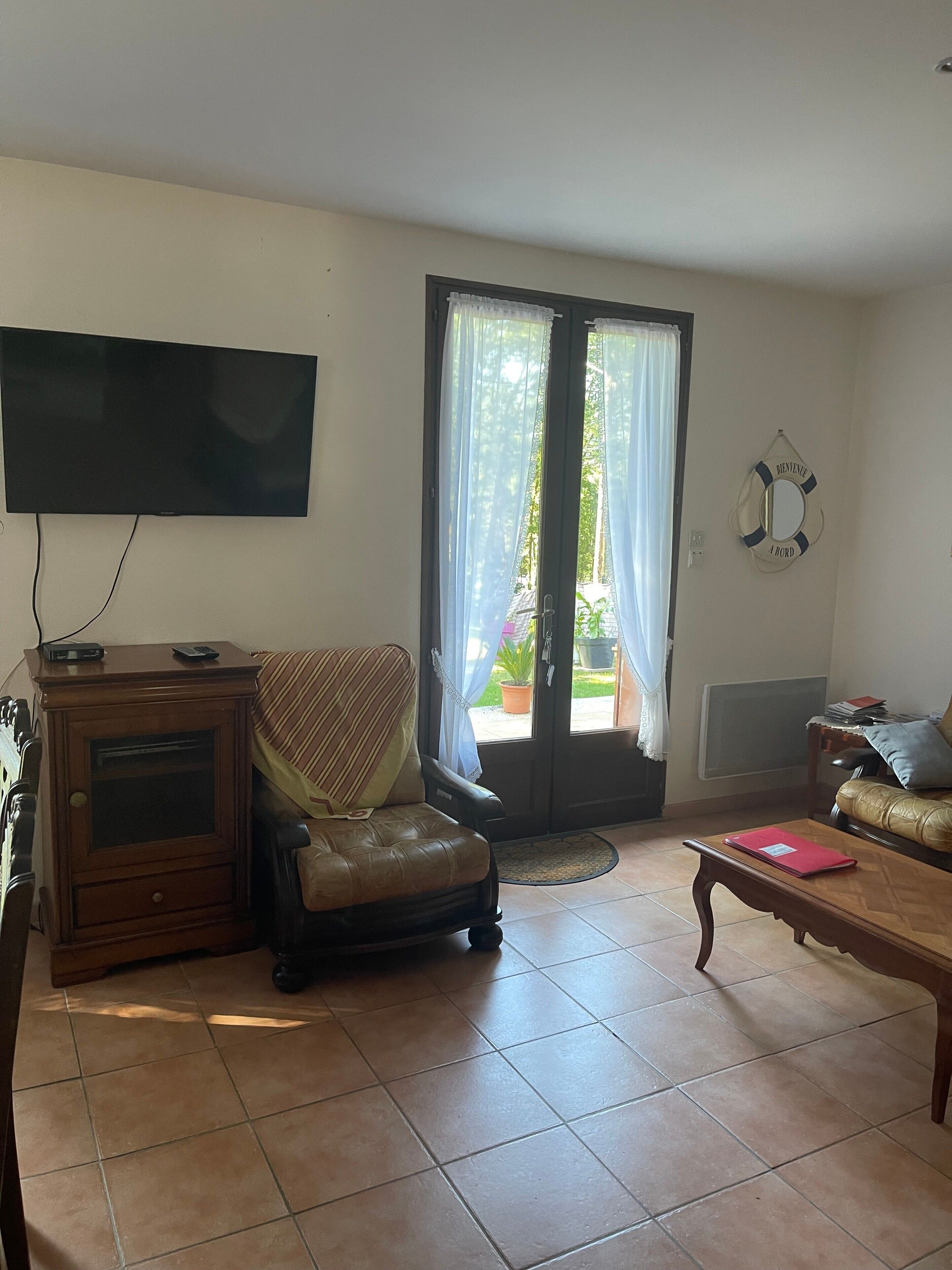 Un salon comprenant un téléviseur, un fauteuil en cuir, une table basse et une porte-fenêtre coulissante donnant sur un balcon.