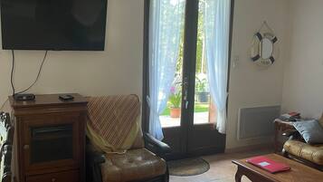 Un salon comprenant un téléviseur, un fauteuil en cuir, une table basse et une porte-fenêtre coulissante donnant sur un balcon.