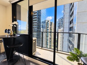 Een balkon met uitzicht op hoge gebouwen, een tafeltje met twee stoelen en een bloempot.