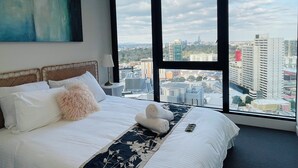 A hotel room with a large bed, a view of the cityscape through large windows, and a painting on the wall. - Southbank 2BR w/ Parking, Balcony & Pool – Walk to Crown (Southbank)