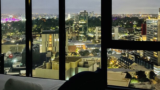 A high-rise hotel room with a large window overlooking a cityscape at night. - Southbank 2BR w/ Parking, Balcony & Pool – Walk to Crown (Southbank)