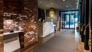 A reception area with a marble counter, brick walls, and a modern chandelier. - Southbank 2BR w/ Parking, Balcony & Pool – Walk to Crown (Southbank)