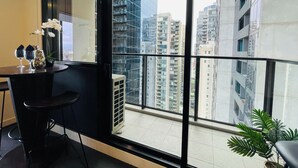 A balcony with a view of high-rise buildings, a small table with two glasses and a decorative vase, and a potted plant. - Southbank 2BR w/ Parking, Balcony & Pool – Walk to Crown (Southbank)