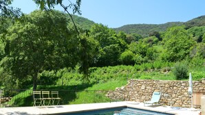 Una piscina con un muro de piedra, dos sillas y un sillón de descanso.