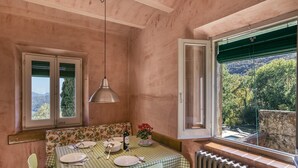 Un comedor con una mesa dispuesta para dos, un radiador, una ventana con vistas a árboles y una lámpara colgante.
