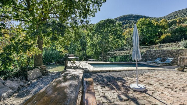 Un banco de madera, una piscina y un muro de piedra.