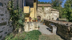 Un patio con un muro de piedra, plantas en macetas y una pequeña estructura de madera.