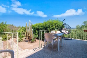 Une terrasse extérieure avec une table et des chaises, entourée de cactus et de verdure, sous un ciel dégagé.