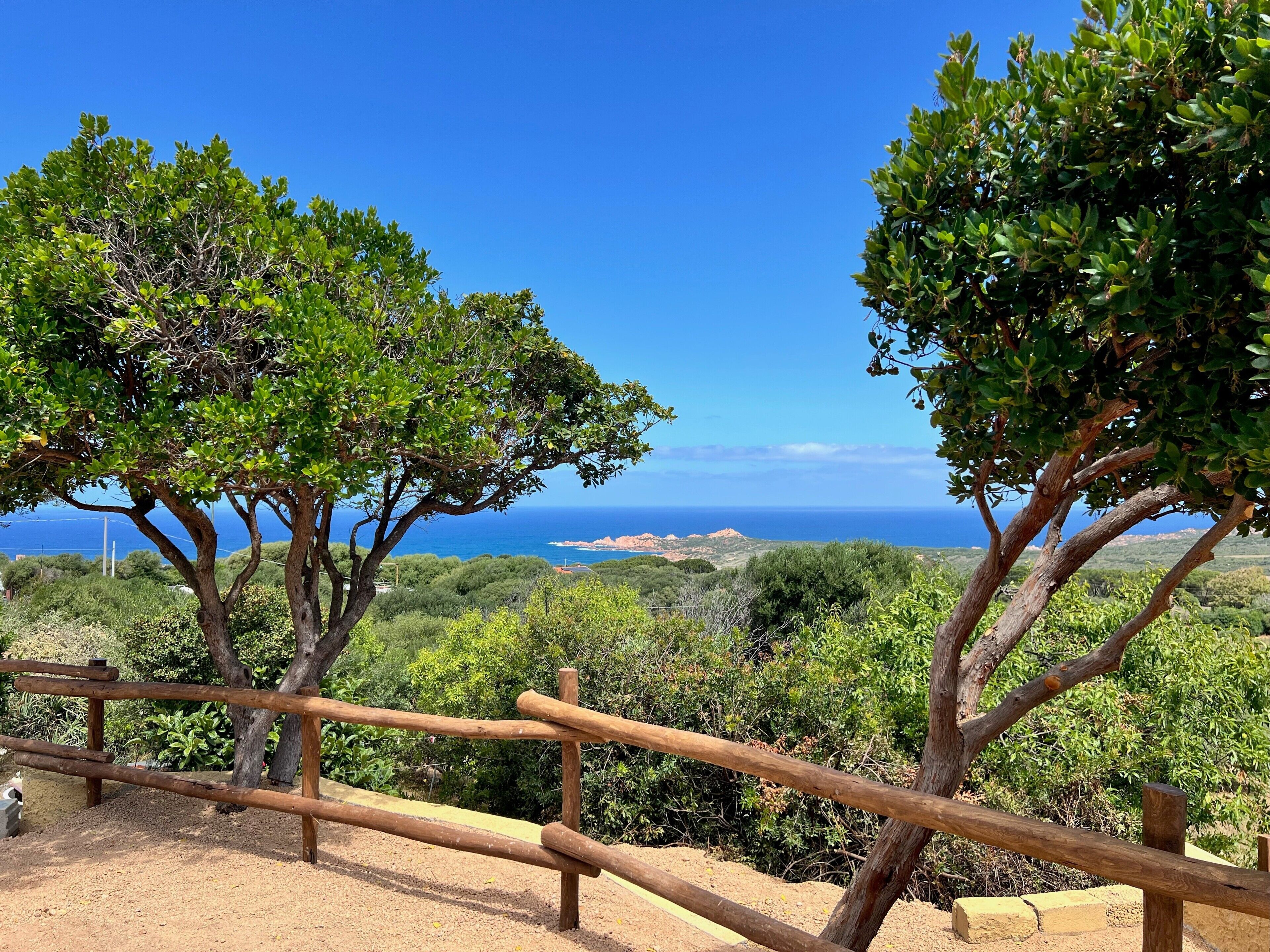 Une clôture en bois, bordée d’arbres, avec vue sur l’océan.