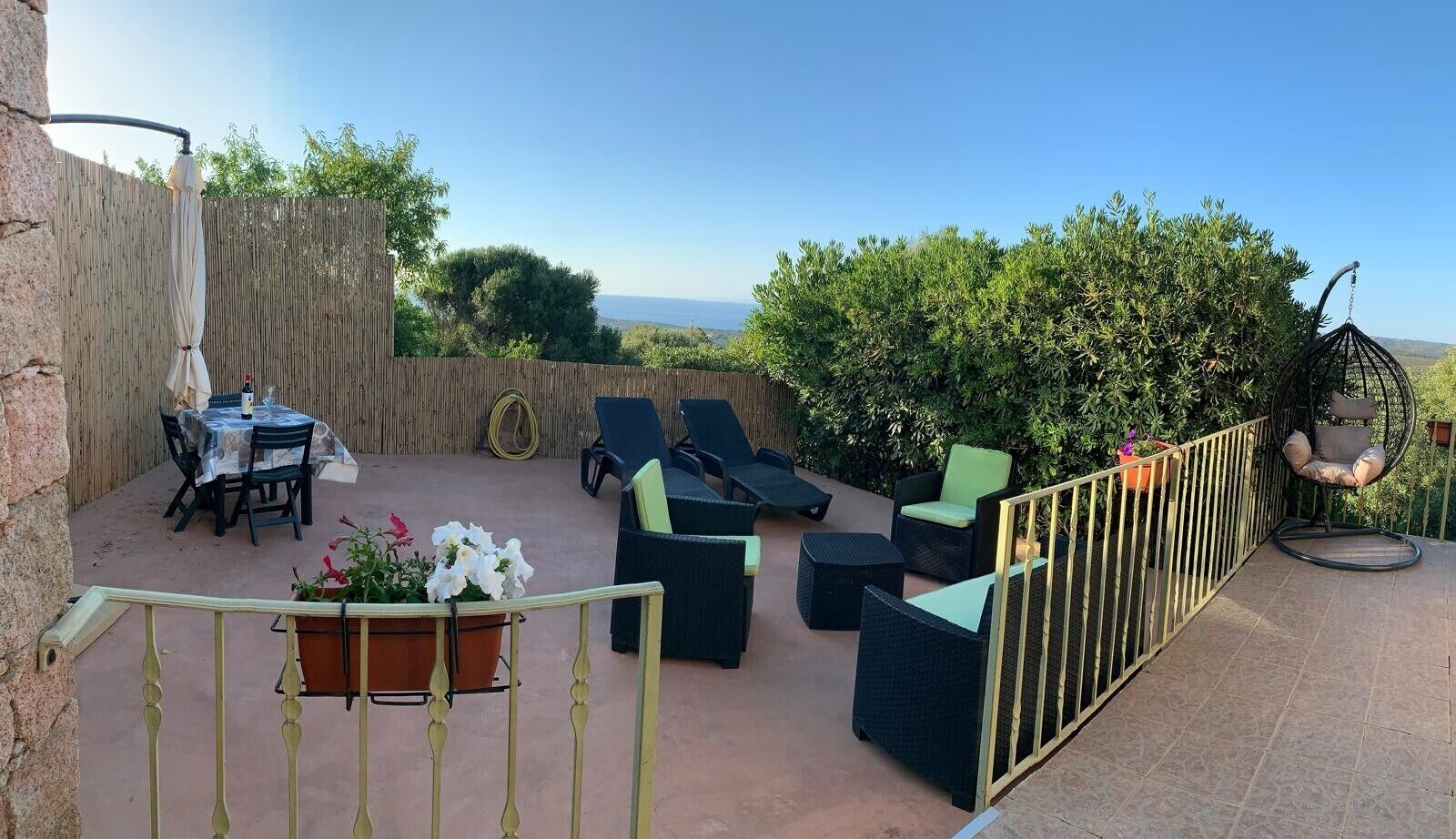 An outdoor patio with a table and chairs, a hanging chair, and a view of the sea.