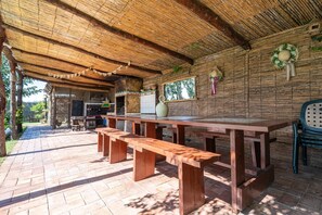 An outdoor dining area with a long wooden table and benches, surrounded by a thatched roof structure. - Holiday Home "Deltaprego" with Private Pool & Wi-Fi (Deltebre)