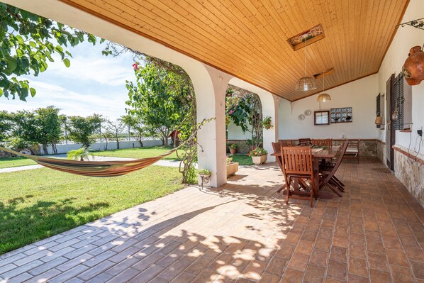 An outdoor patio with a wooden ceiling, a dining table with chairs, and a hammock.