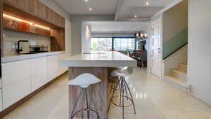Una cucina moderna con isola centrale, sgabelli da bar e una scala che conduce a un altro livello.