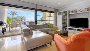 Un soggiorno moderno con un divano componibile, un tavolino, una televisione e un balcone con mobili da esterno.