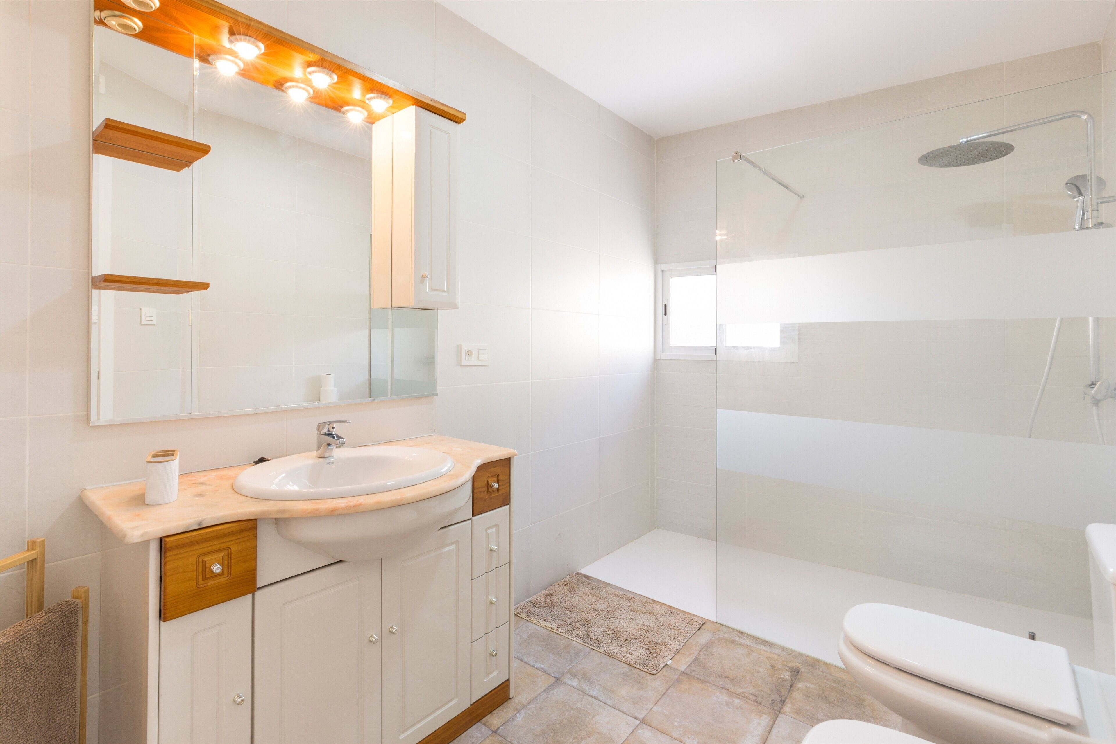 Un baño moderno con lavamanos, espejo e inodoro con ducha.