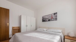 Quarto com cama, guarda-roupa, cadeira, mesa de cabeceira e um quadro na parede da Torre Eiffel.