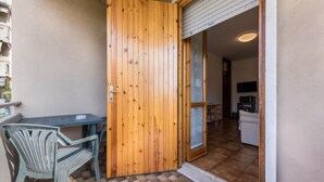 Uma porta de madeira que dá para um quarto com chão de azulejos, uma mesa e uma cadeira.