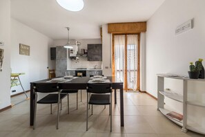 A modern kitchen with a dining table, chairs, and a white shelf with plants.