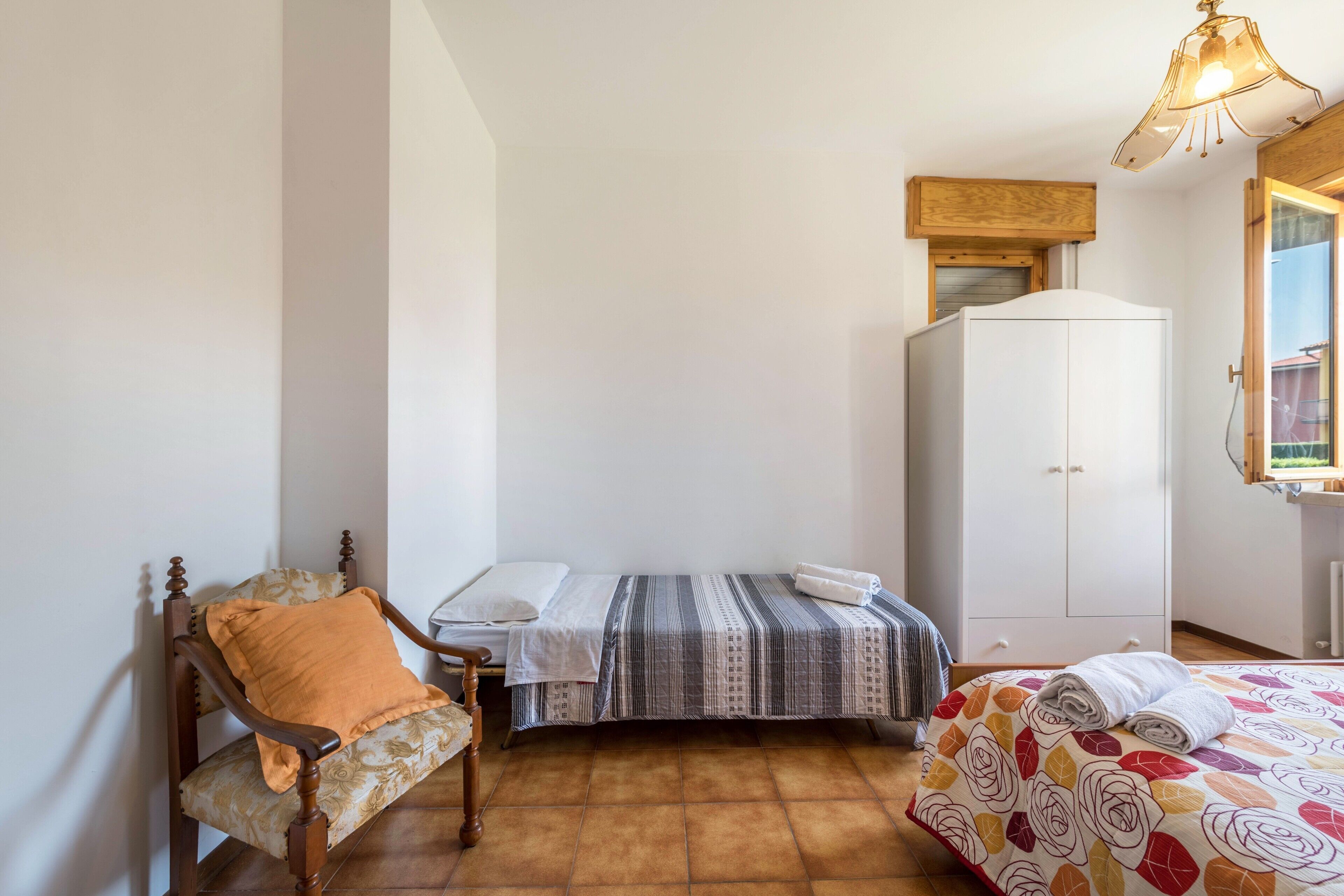 A bedroom with a bed, a chair, a wardrobe, and a window.