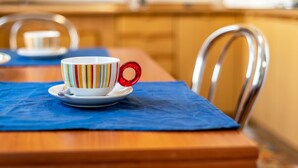 Una mesa de comedor con una taza y platillo a rayas de colores, un mantel azul y una silla de metal.