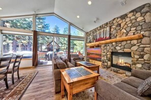 A cozy living room with a stone fireplace, large windows, and a view of a cabin.