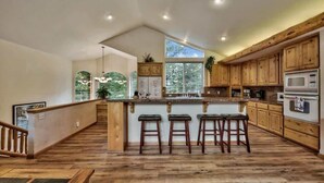 Una cocina amplia con armarios de madera, una isla central con taburetes y vistas al exterior a través de ventanas grandes.