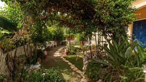 A garden pathway leading to a covered seating area with chairs and tables.