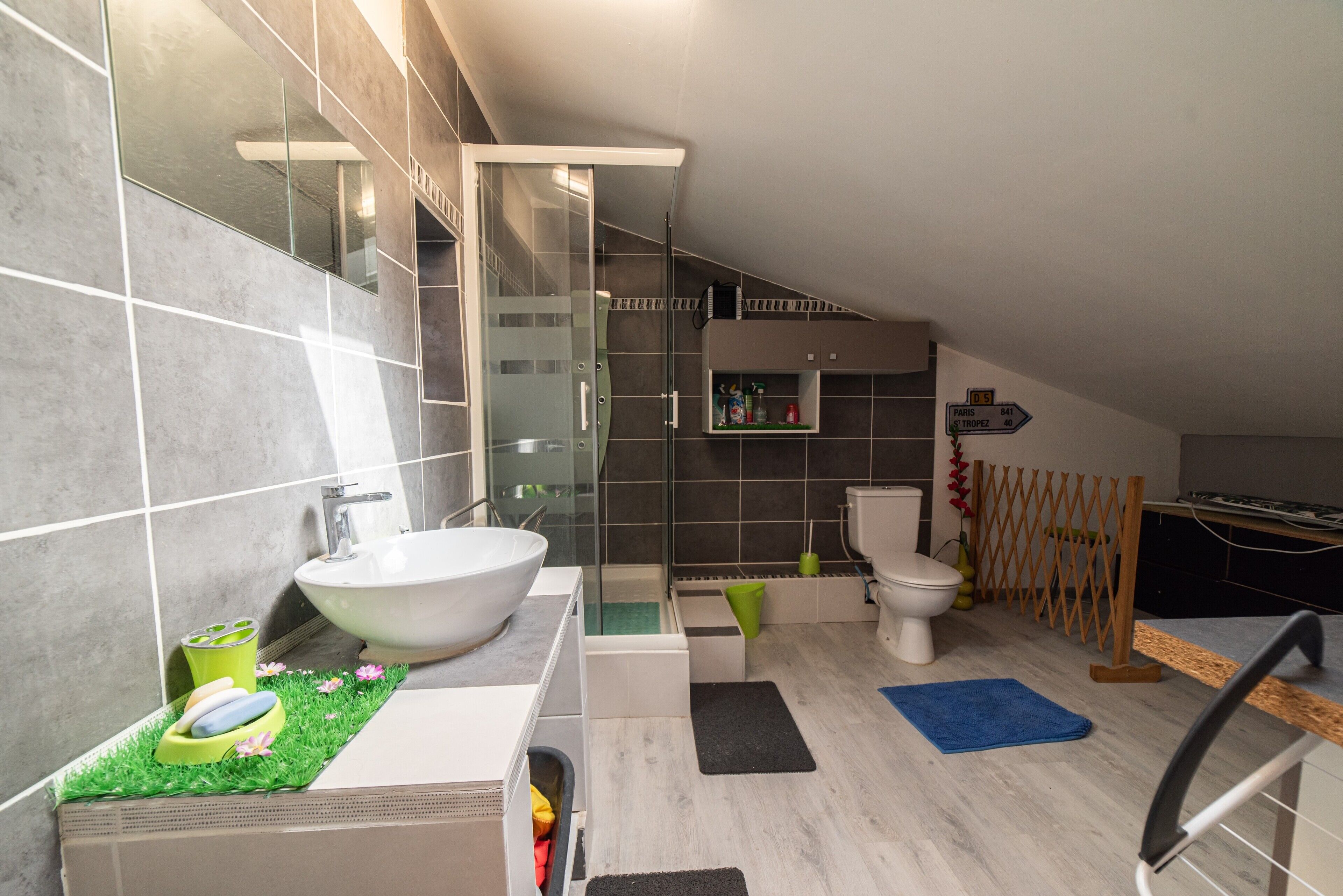Une salle de bain moderne avec un grand lavabo blanc, une cabine de douche en verre, des toilettes et un espace douche agrémenté d’un treillis en bois.