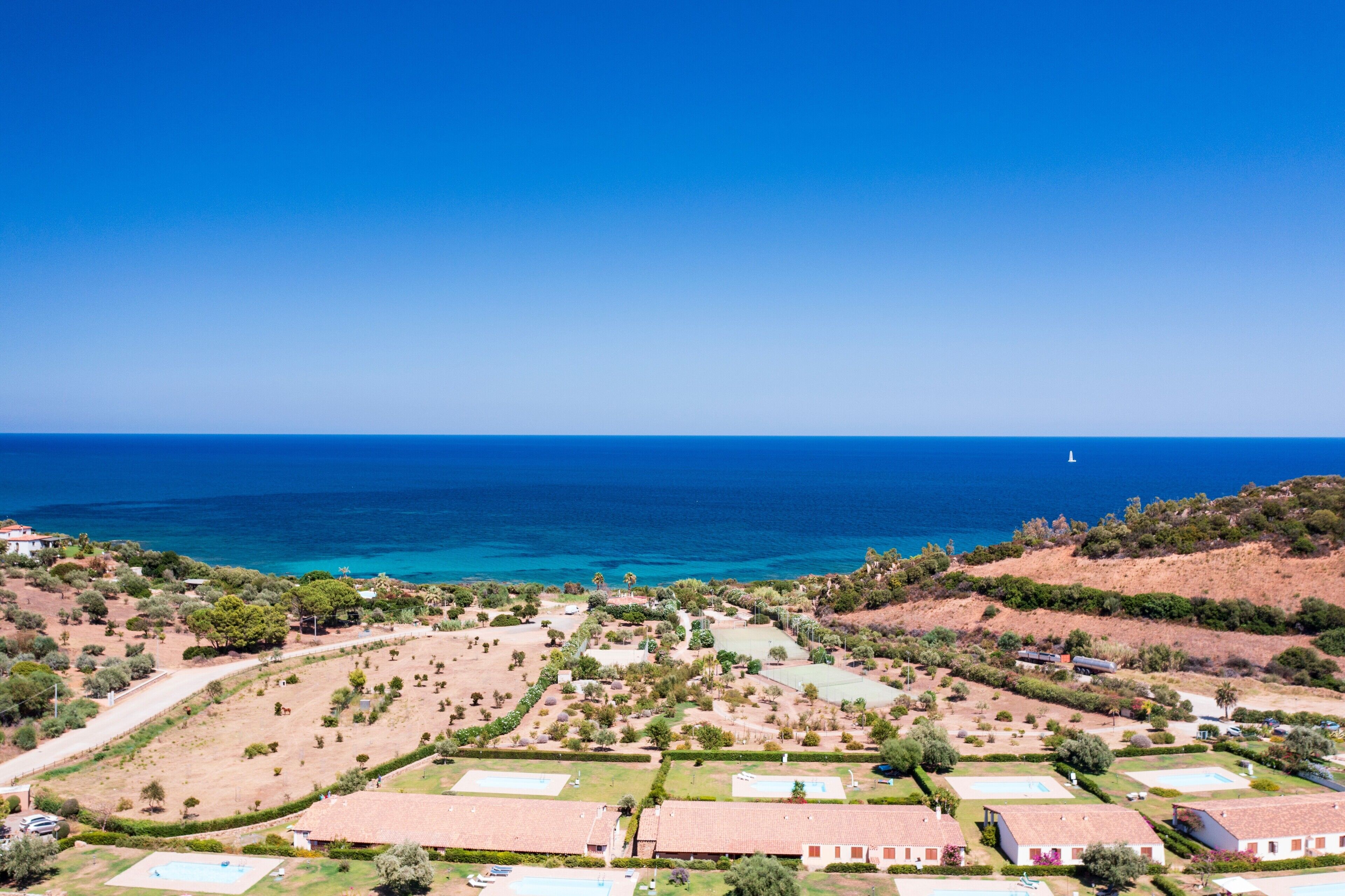 Une vue aérienne d’une zone côtière, avec des bâtiments, des espaces verts et un ciel bleu dégagé.