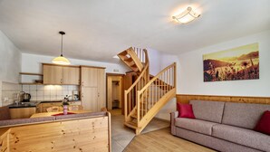 A modern kitchen with wooden cabinets, a dining area, a wooden staircase, a sofa, and a painting on the wall.