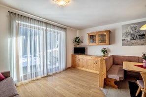 Una sala de estar con sofá, una mesa de comedor de madera, un mueble aparador y un televisor sobre un soporte.
