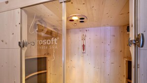 A sauna room with wooden walls, a glass door, and a visible thermometer.