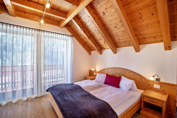 Une chambre avec un plafond en bois, un lit avec une literie blanche, un plaid noir et deux tables de chevet avec des lampes.