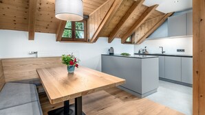 A modern kitchen with wooden beams, a central island, and a dining area with a bench and table. - Apartment "Perfila Dolomitenblick" with Mountain View, Shared Garden & Wi-Fi (Valdaora)