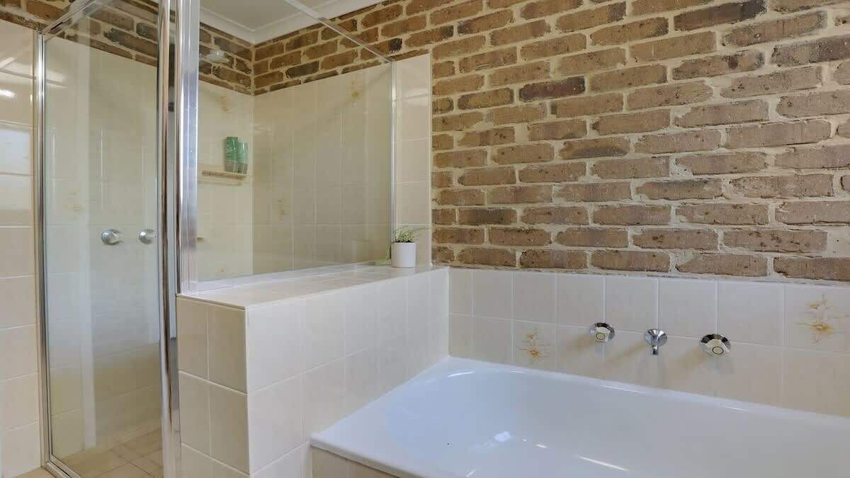 Un bagno con cabina doccia in vetro, una vasca da bagno bianca e un muro in mattoni.