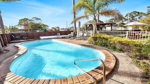 Una piscina con bordo in legno, lettini e un'area recintata con palme.