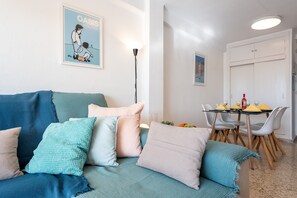 Una sala de estar con un sofá, cojines, una mesa con sillas y un comedor.