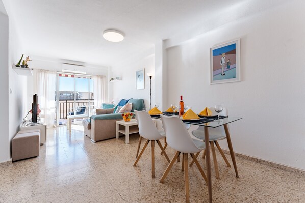 A modern living room with a dining area, a sofa, a TV, and a balcony with a view.