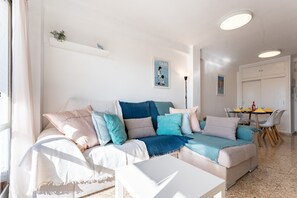 Una sala de estar con sofá, una mesa de centro, un comedor con sillas y una zona de cocina con mesa y sillas.