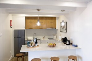 Une cuisine moderne dotée d’un îlot central, d’appareils électroménagers en acier inoxydable, de meubles en bois, de luminaires suspendus et d’un petit coin salon avec des tabourets.
