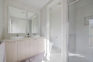 Une salle de bain moderne avec un grand miroir, deux lavabos, des toilettes et une douche à parois de verre.