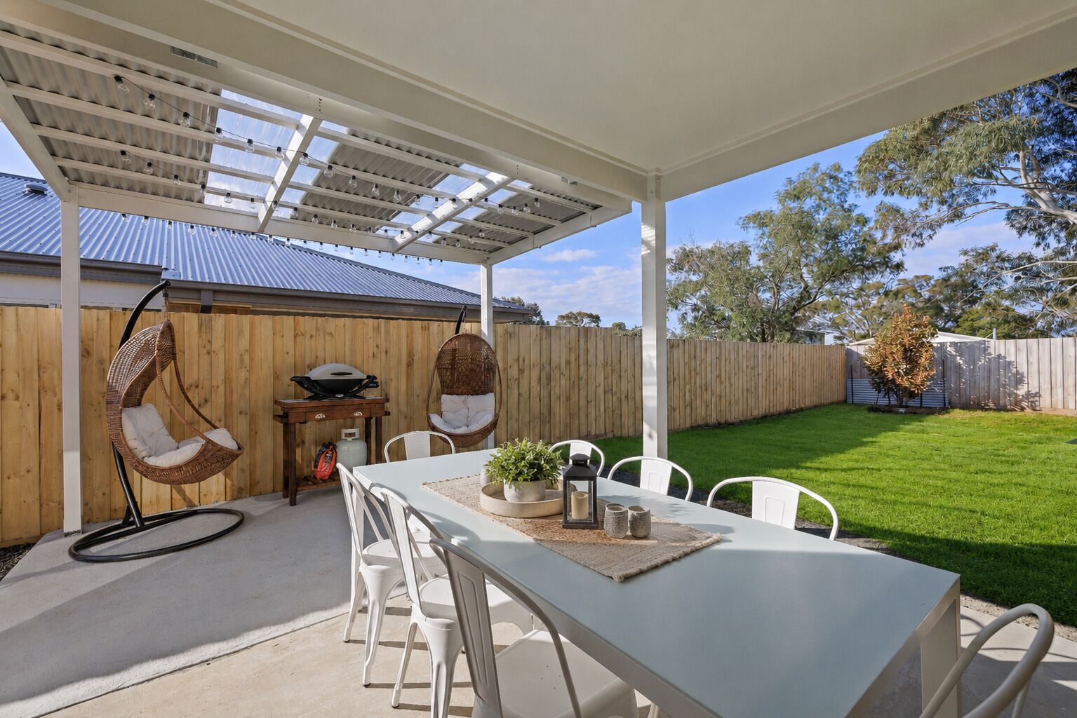 Un patio al aire libre con una mesa, sillas, sillones colgantes y una parrilla.