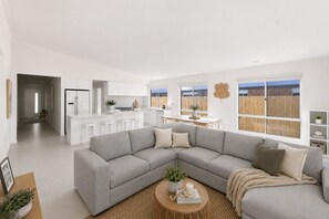 A modern living room with a grey sectional sofa, a coffee table with decorative items, and a view of a kitchen and dining area through large windows. - Shore to Please by Ready Set Stay - Family-friendly and WIFI (Cowes)