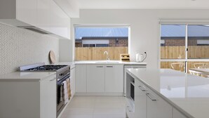 A modern kitchen with white cabinetry, a gas stove, and a large window overlooking a wooden fence.