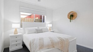 A white bedroom with a bed, two bedside tables, a window, and a wall-mounted circular shelf.
