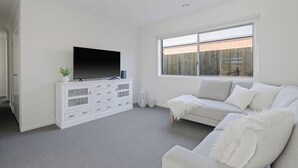 A modern living room with a flat-screen TV on a white cabinet, a grey sofa, and a large window with a view of a brick wall.