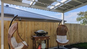 A covered patio area with two wicker chairs, a gas grill, and a small table.