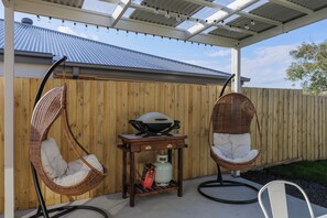 Un patio couvert comprenant deux fauteuils en osier, un barbecue au gaz et une petite table.