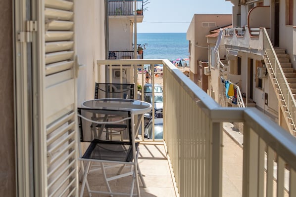 Un balcón con mesa y sillas, con vistas a la playa y edificios cercanos.